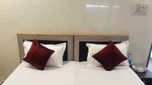 Una cama doble con dos almohadas, una toalla enrollada y una colcha roja.