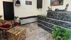Un área de recepción con mostrador de mármol, mobiliario de mimbre, plantas en macetas y decoración en la pared.