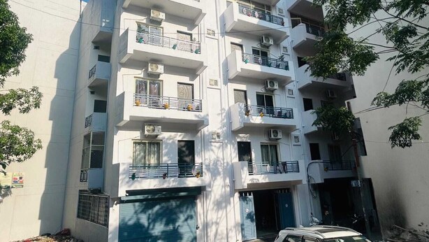 Un edificio residencial de varios pisos con balcones, unidades de aire acondicionado y una entrada con portón.