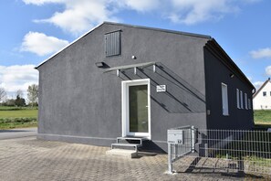 Un bâtiment moderne avec une façade grise, une porte blanche et une clôture en métal à l’avant.