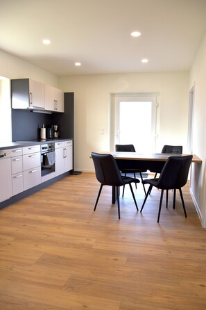 Une cuisine moderne avec des meubles blancs, une table à manger en bois et des chaises noires.