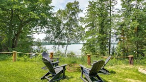 Två Adirondack-stolar placerade framför en sjö, med ett rep som avgränsning och träd i bakgrunden.