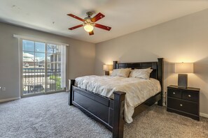 Une chambre à coucher comprenant un lit, deux lampes de chevet, une table de chevet, un ventilateur de plafond et une grande fenêtre donnant sur un beau paysage.