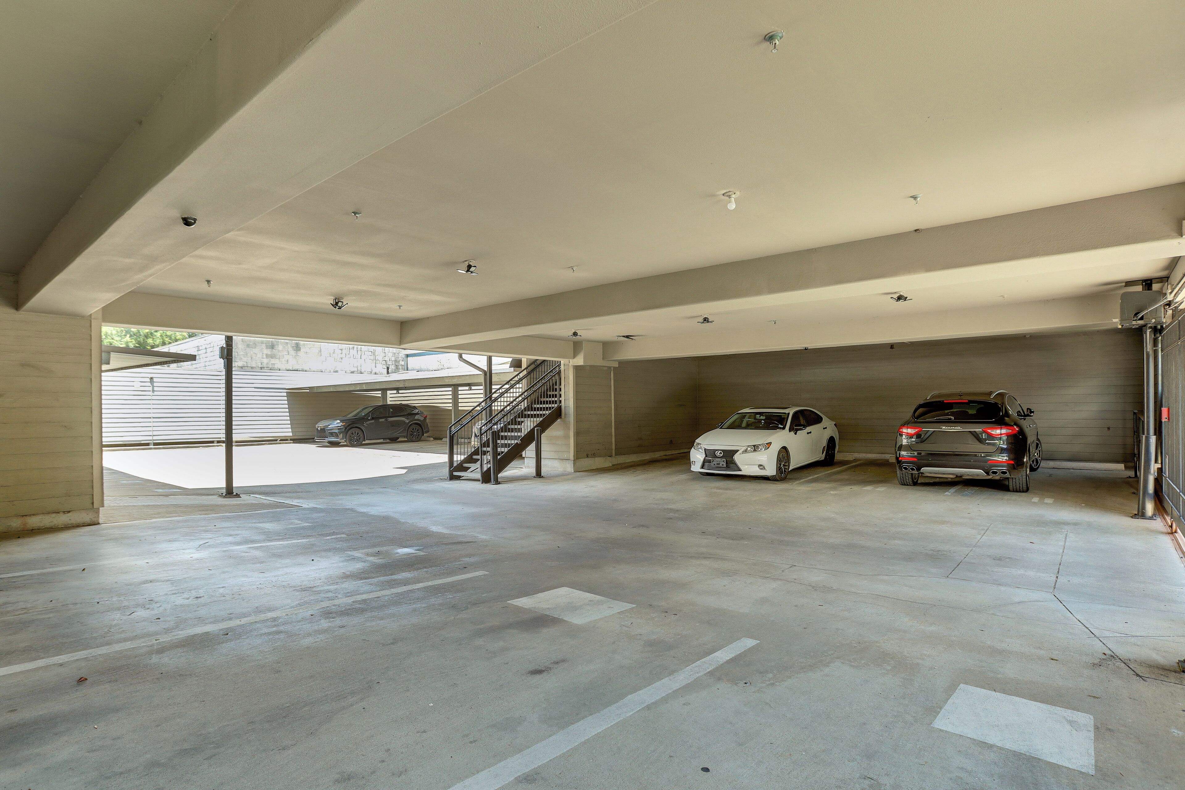 Eine überdachte Tiefgarage mit Betonböden, einer Treppe und zwei parkenden Autos.