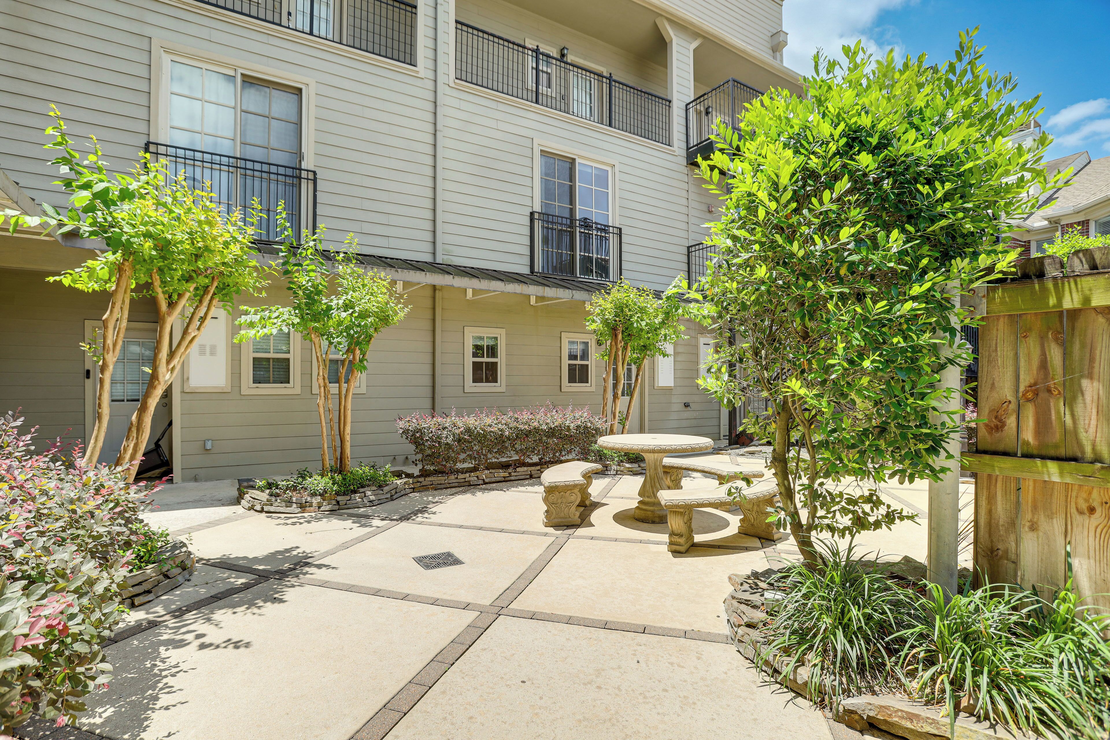 A courtyard with a stone table and benches, surrounded by plants and trees.