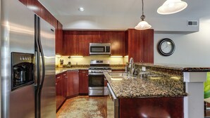 Una cocina con electrodomésticos de acero inoxidable, encimeras de granito, armarios de madera e iluminación colgante.