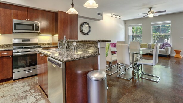Una cocina moderna con electrodomésticos de acero inoxidable, encimera de granito y comedor con mesa de vidrio y sillas de metal.