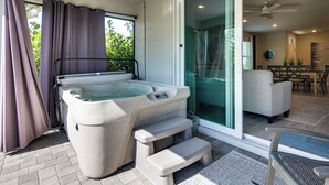 Ein Whirlpool mit Stufen, eine Glastür zu einer Terrasse und ein Deckenventilator.