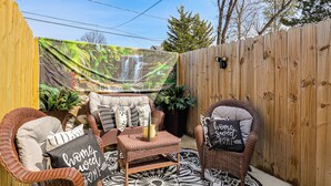 Ein Patio mit Korbmöbeln, einem gemusterten Teppich und einem Wandbild einer Wasserfallansicht.