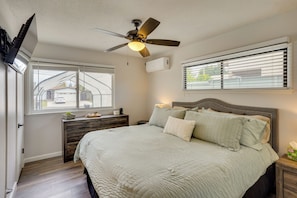 Ein Schlafzimmer mit Bett, Deckenventilator, Fenster mit Jalousien, Nachttisch und Kommode.