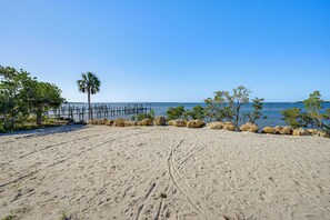 Ein sandiger Strand mit einer Holzsteg, Palmen und einem wolkenlosen, blauen Himmel.