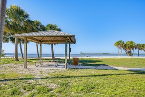 Ein Park direkt am Strand mit einem hölzernen Pavillon, Picknicktischen und einem Mülleimer.