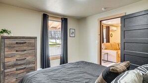 A bedroom with a bed, a wooden dresser, a window with curtains, and a view of an outdoor area.