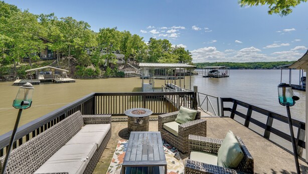 Eine Terrasse mit Gartenmöbeln, einer Feuerstelle und Blick auf das Wasser sowie die umliegenden Gebäude.