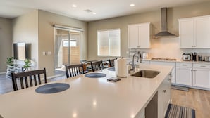A modern kitchen with white cabinets, a large island, and a dining area with chairs and a table. - 9 Mi to Las Vegas Strip! Spacious Single-Story Gem (Las Vegas)