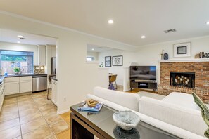 A modern living room with a fireplace, a dining area with a kitchen in the background, and a large window. - Sleek Family Home w/ Backyard Oasis in San Diego! (San Diego)