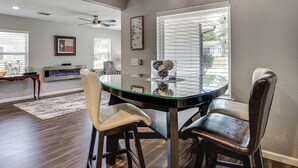A dining area with a glass table, two chairs, a ceiling fan, and a fireplace. - 2 Mi to Stadiums & UT Arlington! Stylish Home (Arlington)