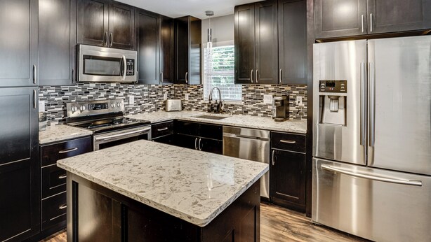 A modern kitchen with dark cabinetry, stainless steel appliances, a marble island, and a tiled backsplash. - 2 Mi to Stadiums & UT Arlington! Stylish Home (Arlington)