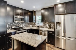 A modern kitchen with dark cabinetry, stainless steel appliances, a marble island, and a tiled backsplash. - 2 Mi to Stadiums & UT Arlington! Stylish Home (Arlington)