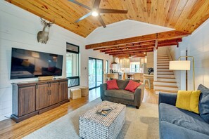 A spacious living area with a wooden ceiling, a television, a sofa, and a staircase leading to an upper level.