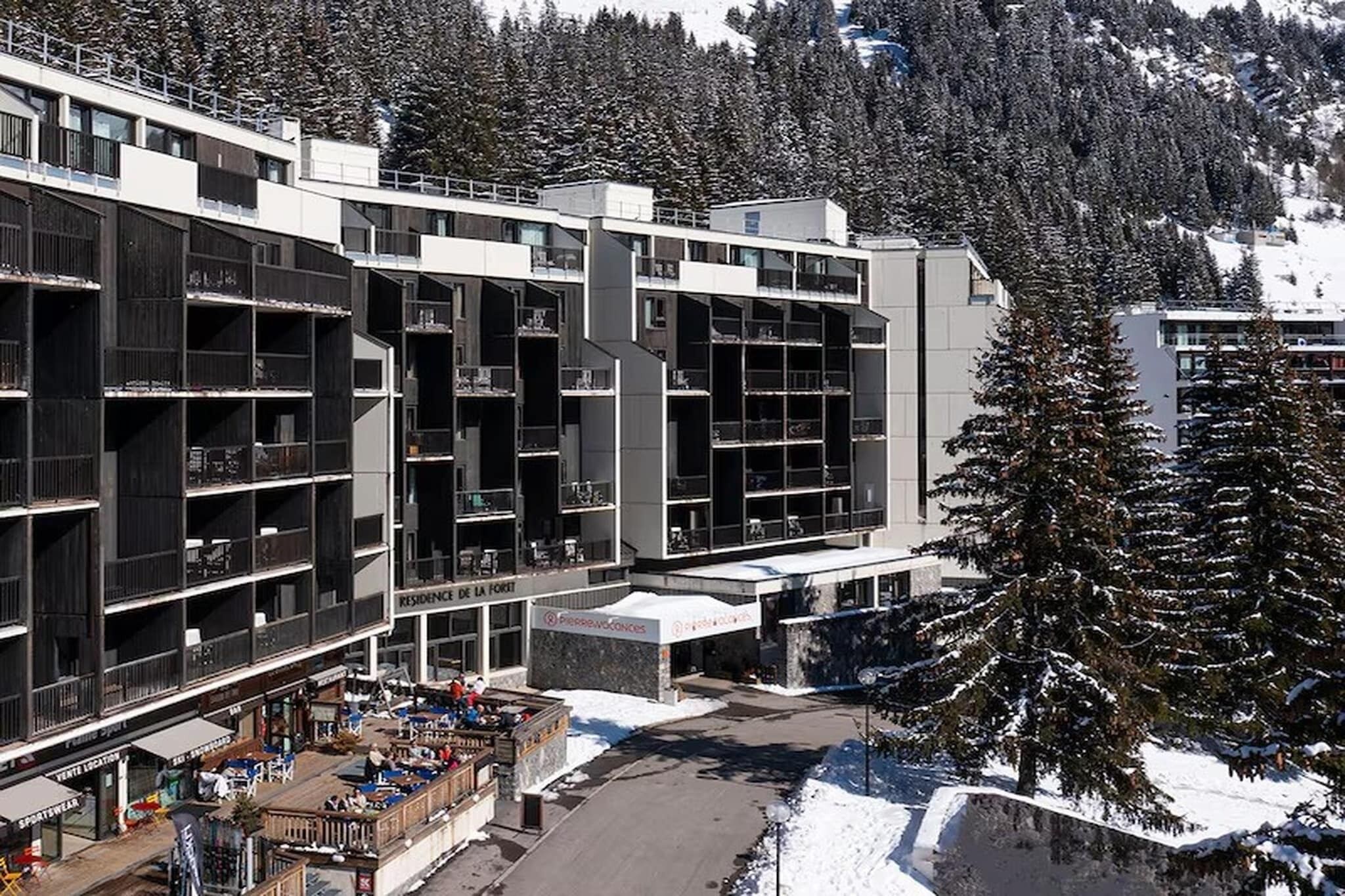A multi-story hotel with balconies, a ski resort in the background, and a snow-covered landscape.