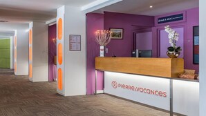 A reception desk with a 'PIERRE&VACANCES' sign, a purple wall, and a wooden counter. - Résidence Pierre & Vacances Mountain view (Flaine)