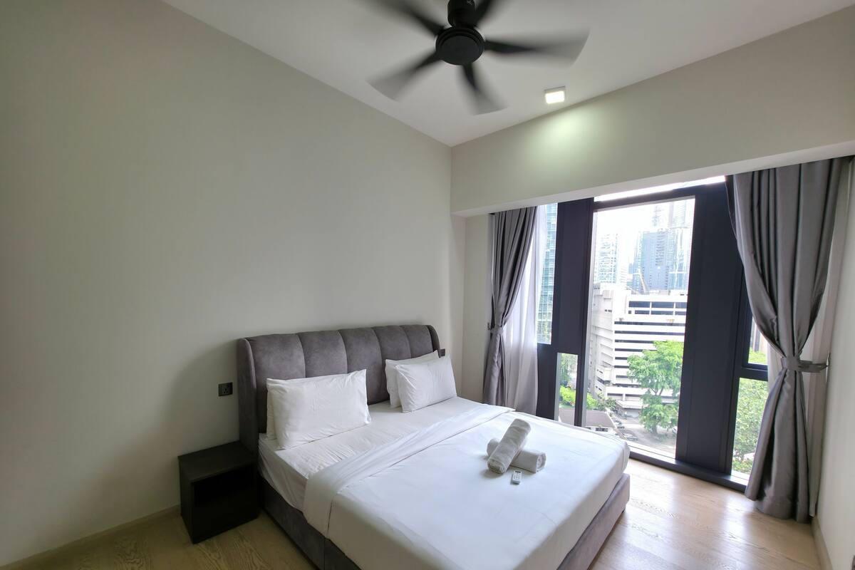 A hotel room with a large bed, a ceiling fan, and a view of the city through the window.