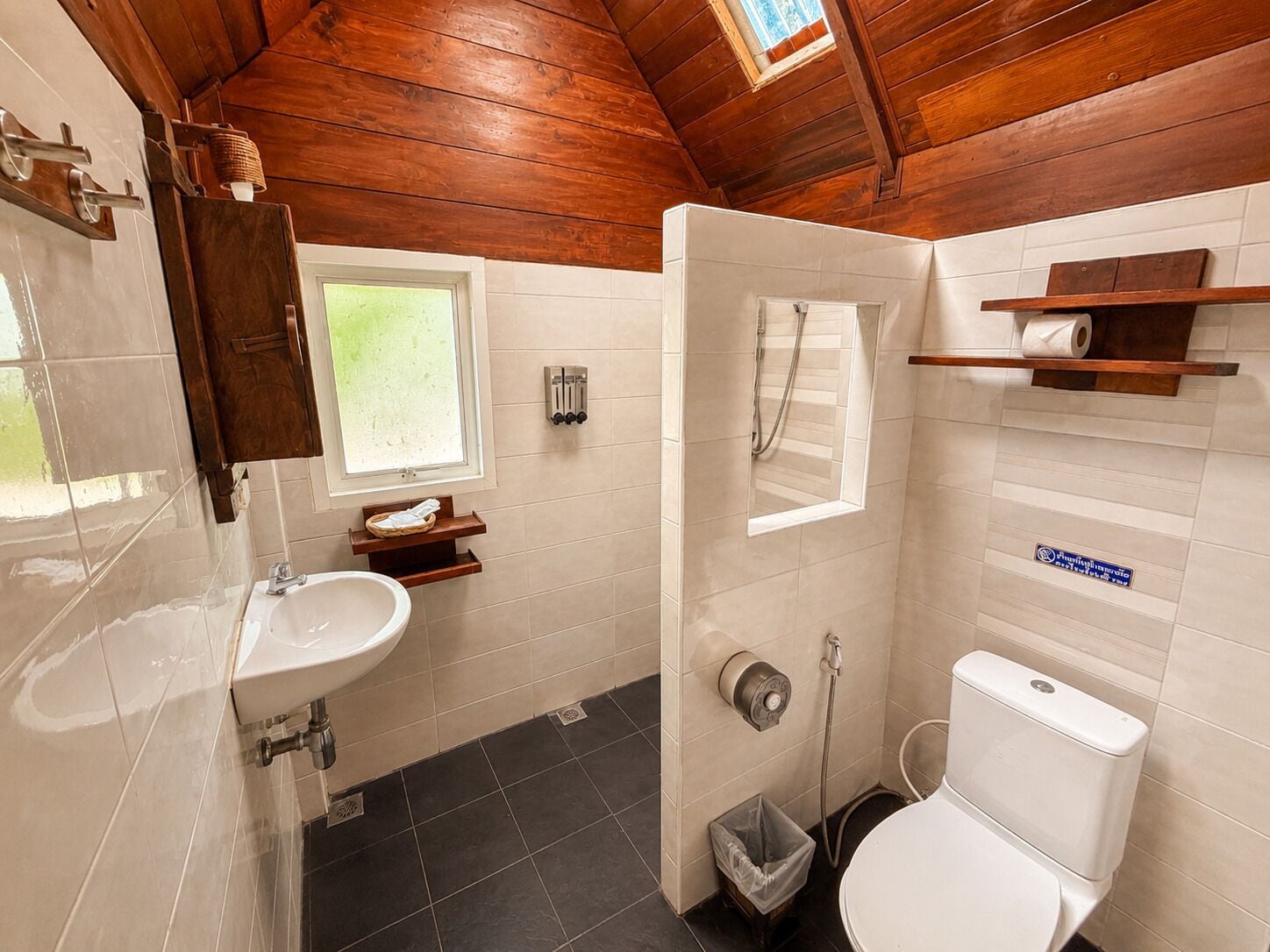 A bathroom with a wooden ceiling, a sink, a toilet, and a shower.