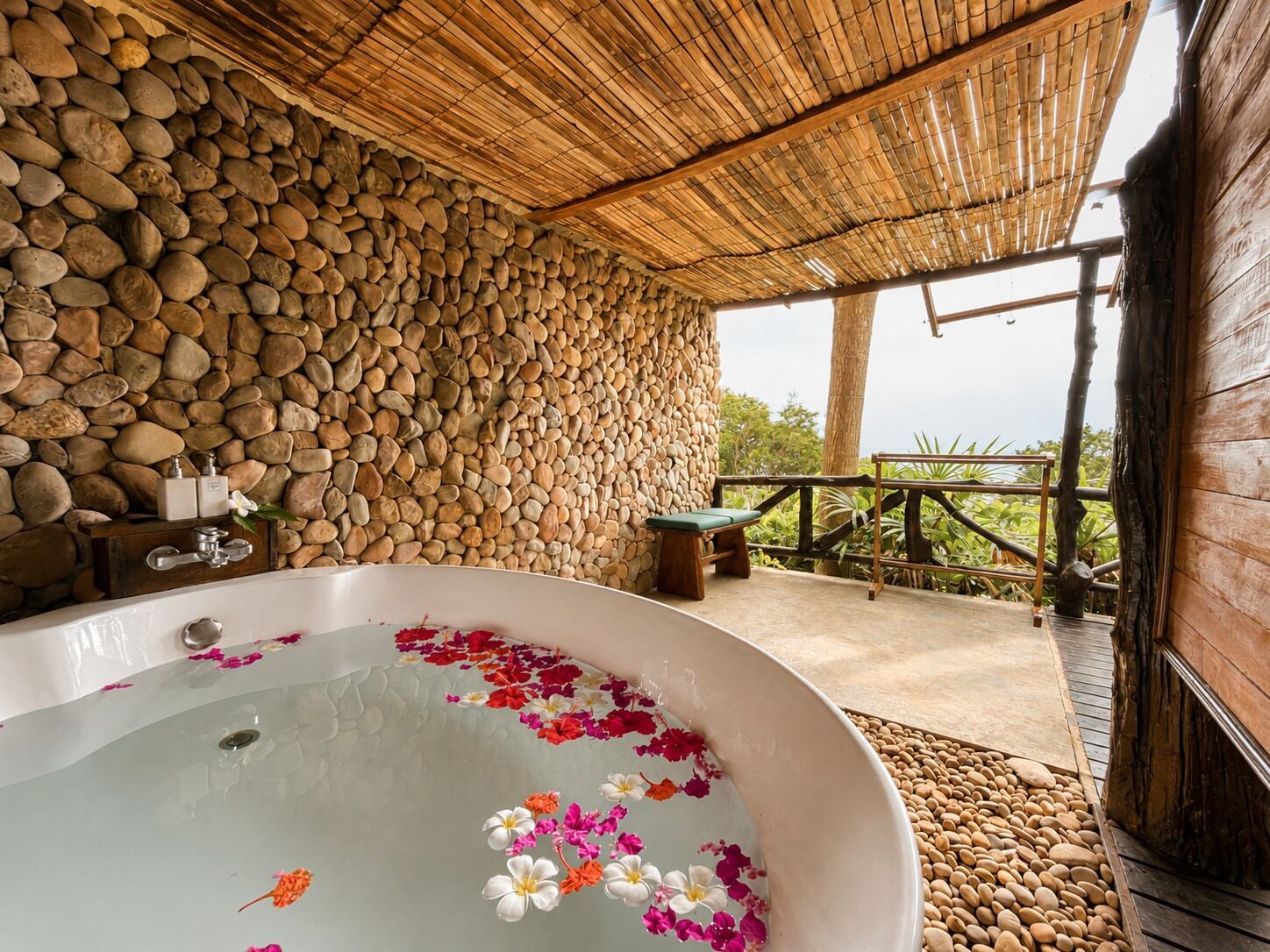 A bathroom with a stone wall, a bathtub with flowers, and a wooden deck.