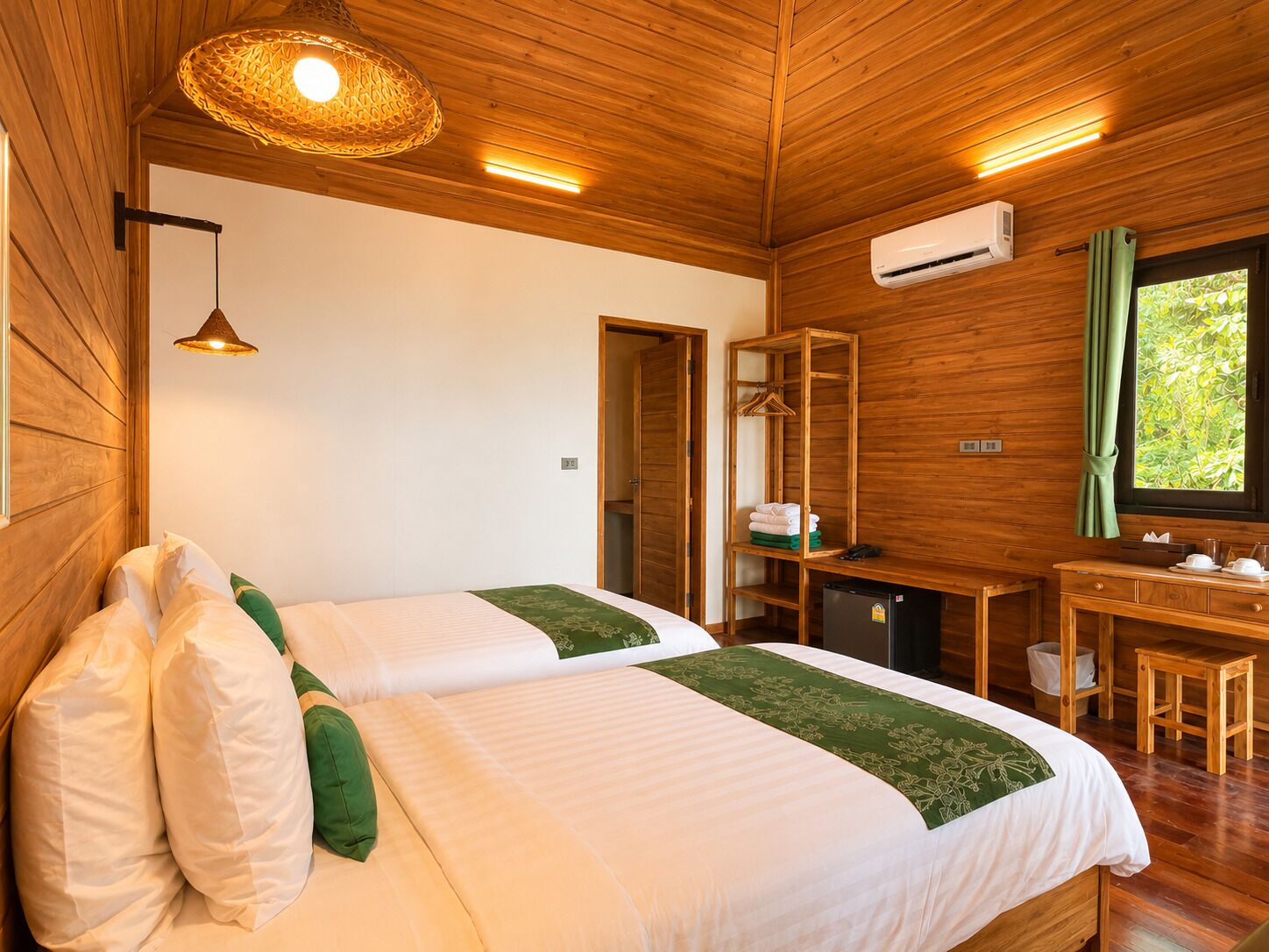 A wooden room with two beds, a desk, and a window with a view.