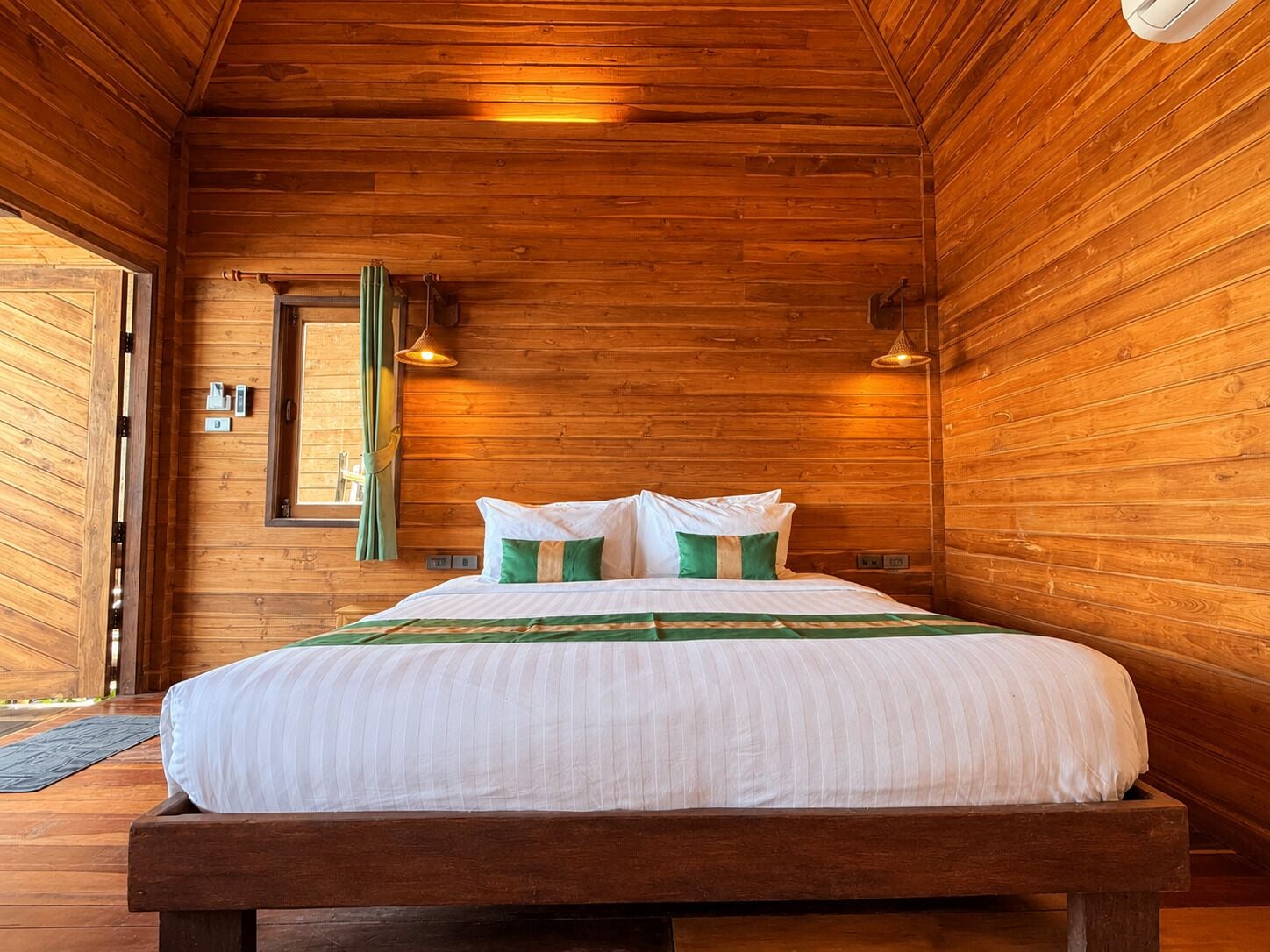 Una habitación de cabaña de madera con una cama, una ventana con cortinas y una puerta.