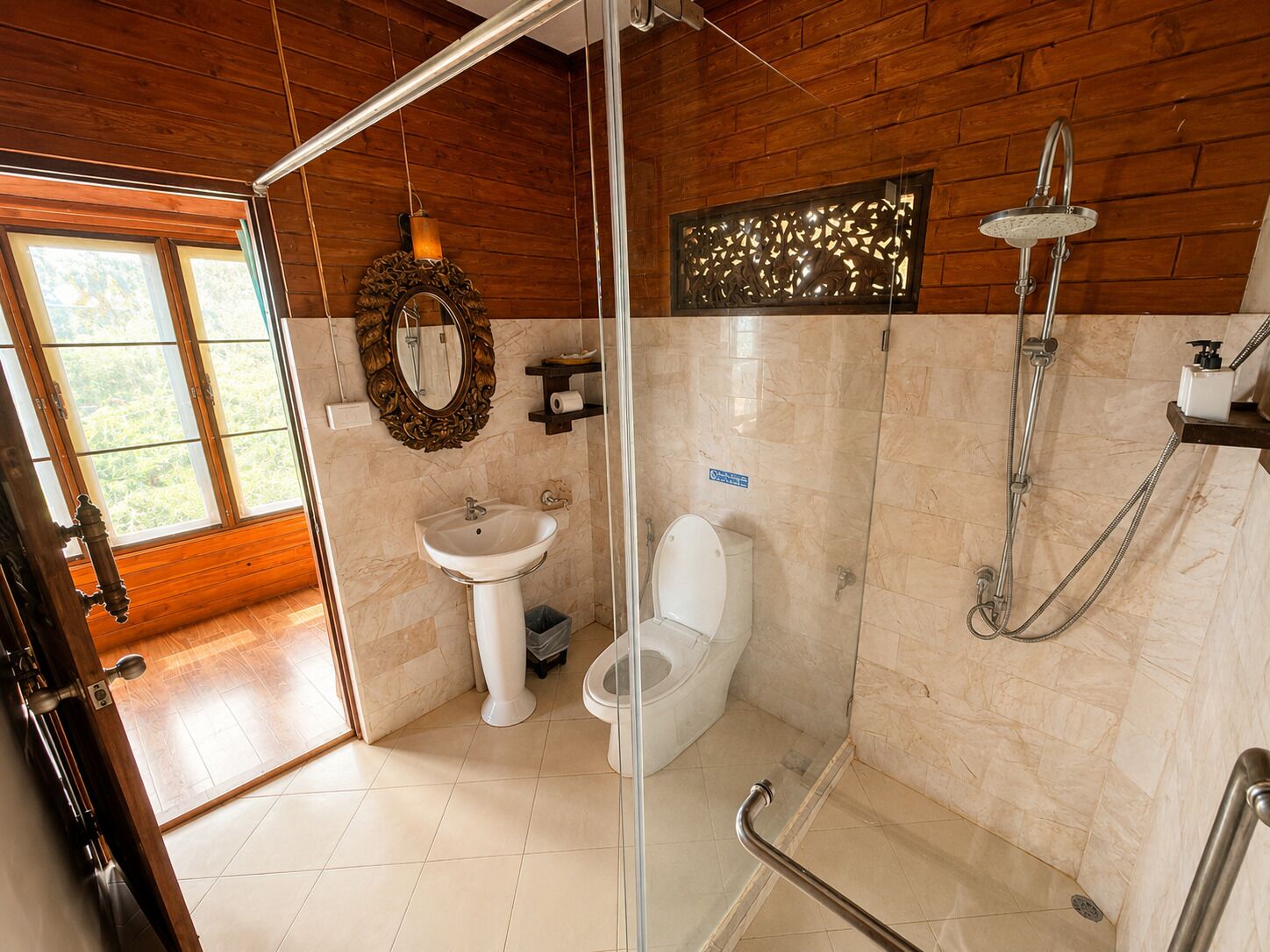 Een badkamer met een wastafel, toilet, douche en een glazen deur die leidt naar een houten kamer.