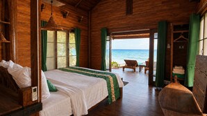 Eine Holzdiele mit Bett, kleinem Tisch und Stuhl. Große Fenster bieten Blick auf den Ozean.
