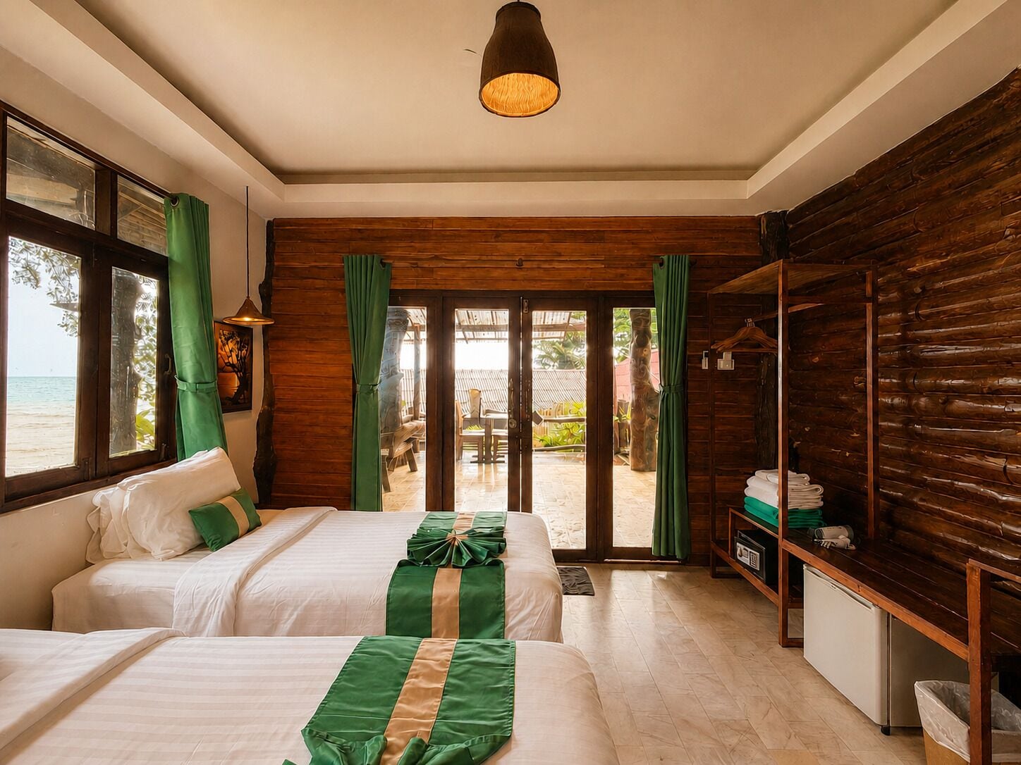 A hotel room with two beds, a desk, a wardrobe, and a view of the beach.