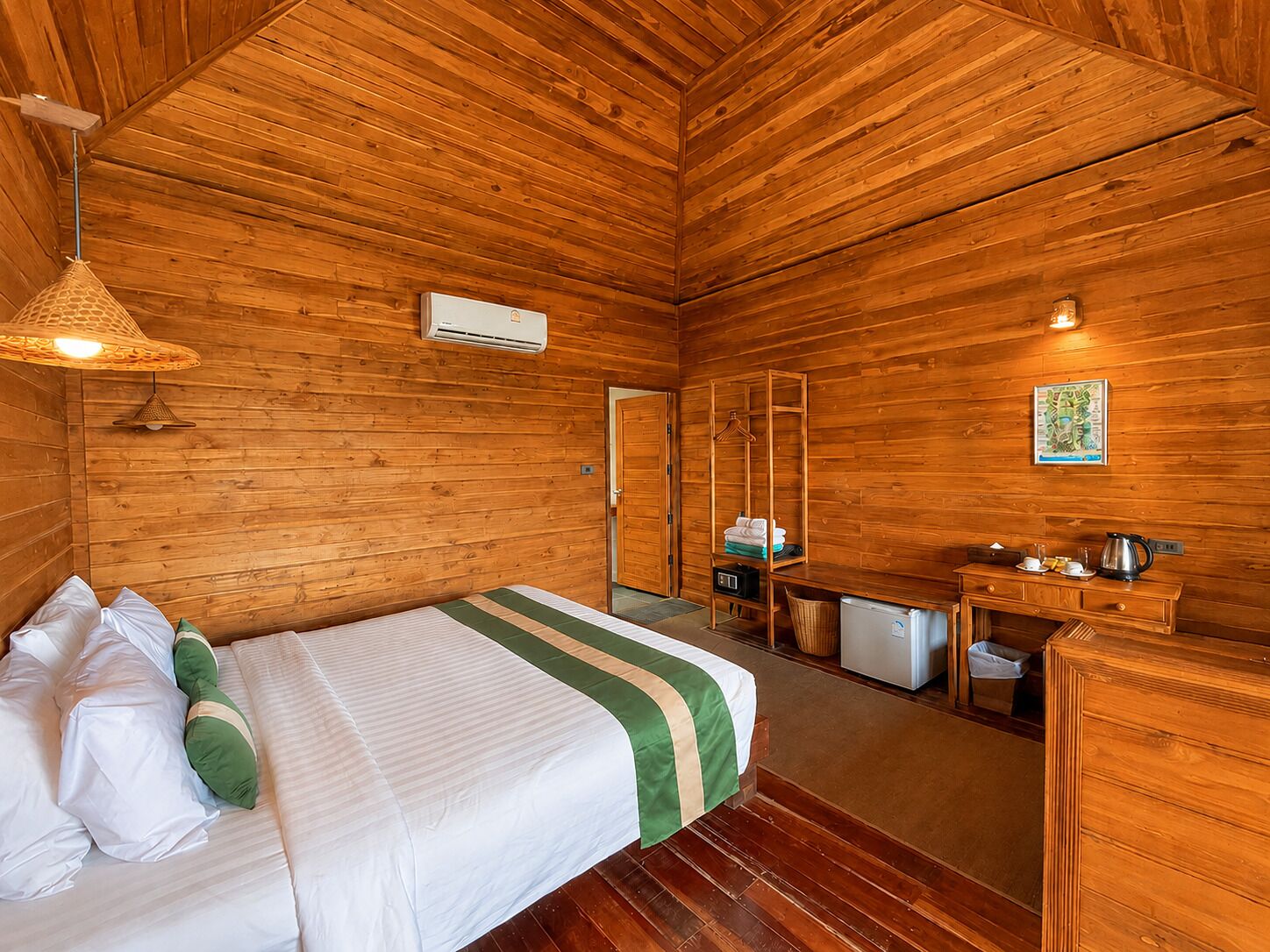 A wooden cabin room with a bed, a desk, a hanging light fixture, and a map on the wall.