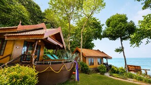 Ein Bungalow mit angedocktem Boot, umgeben von üppiger Vegetation und Blick aufs Meer.