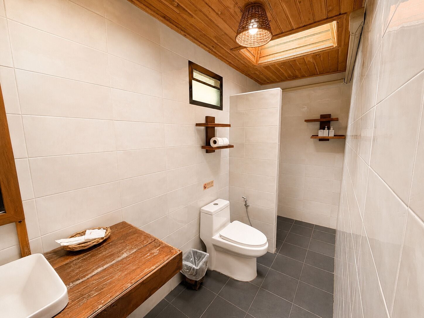 A bathroom with a wooden vanity, a toilet, a shower, and a hanging light fixture.