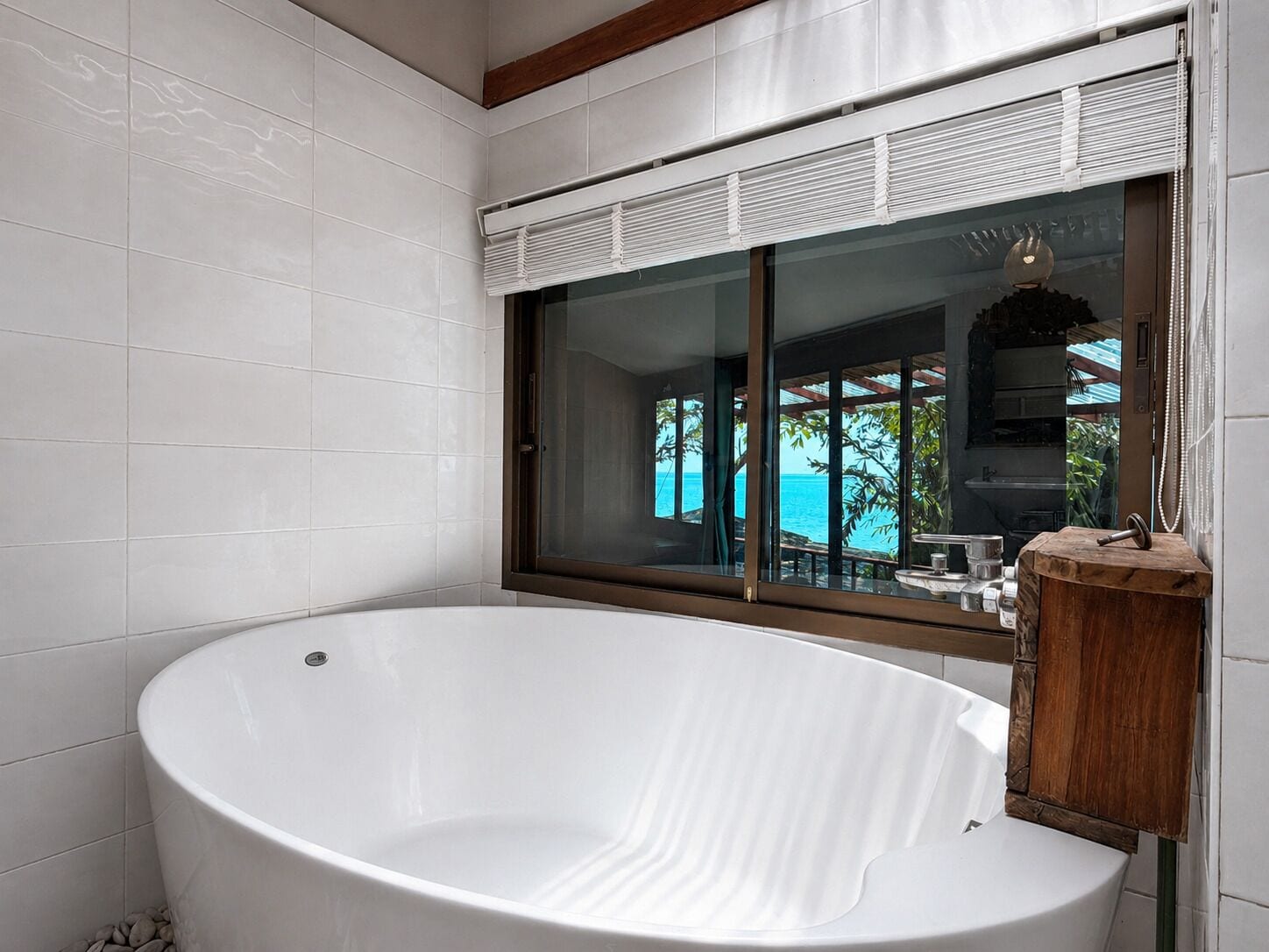 Un baño con una bañera grande, una ventana con persianas y vista al mar.