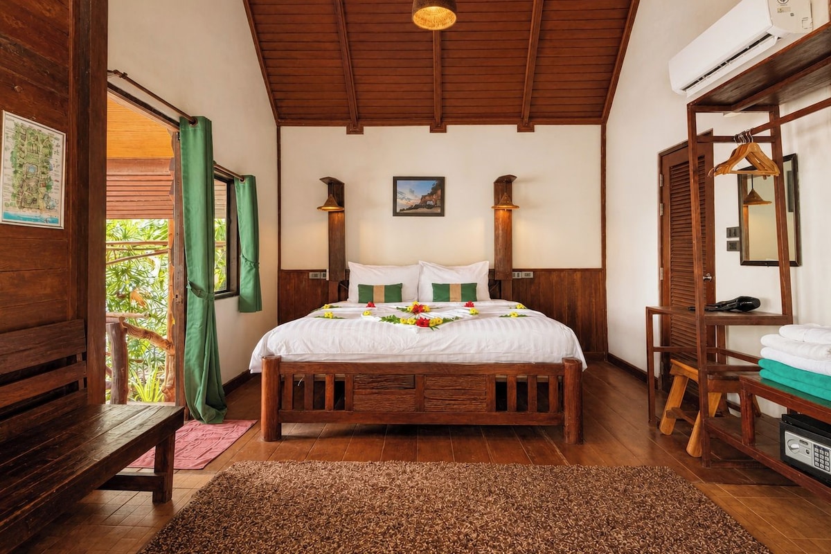 A wooden-framed room with a bed, a bench, a hanging light fixture, and an air conditioning unit.