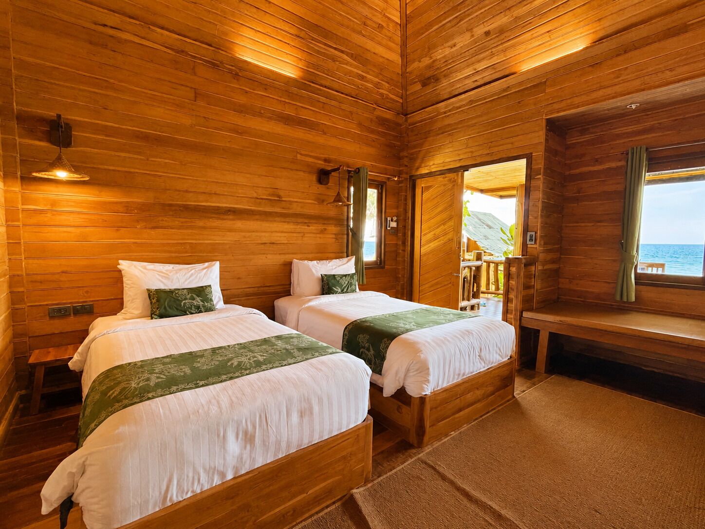 A cabin with two wooden beds, a bench, and a view of the sea.