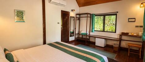A bedroom with a large bed, a desk, and a window with a view of greenery.