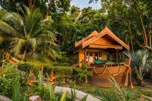 Una casa de madera con balcón, rodeada de abundante vegetación y plantas tropicales.