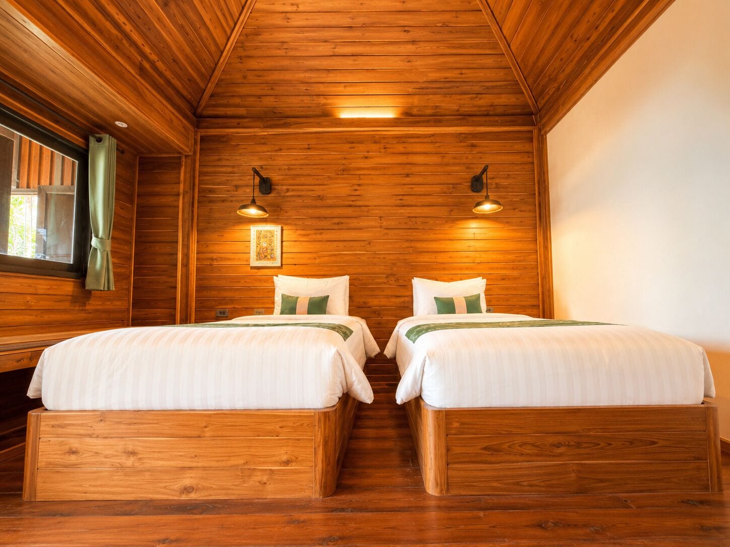 Een houten kamer in blokhutstijl met twee bedden, een raam met gordijnen en twee wandlampen.
