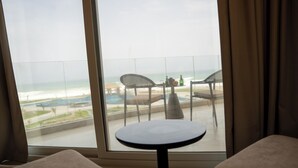Una habitación con un ventanal grande que da a una playa, una mesa redonda y dos sillas.