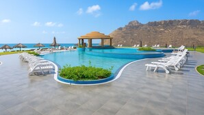 Zona de piscina con sillones de descanso, una pérgola y vista al océano.