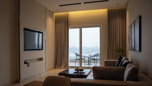 Habitación de hotel moderna con televisor de pantalla plana, sofá, mesa de centro y balcón con vistas al mar.