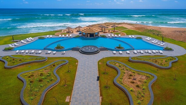 Un resort con piscina central, tumbonas y vista al océano.