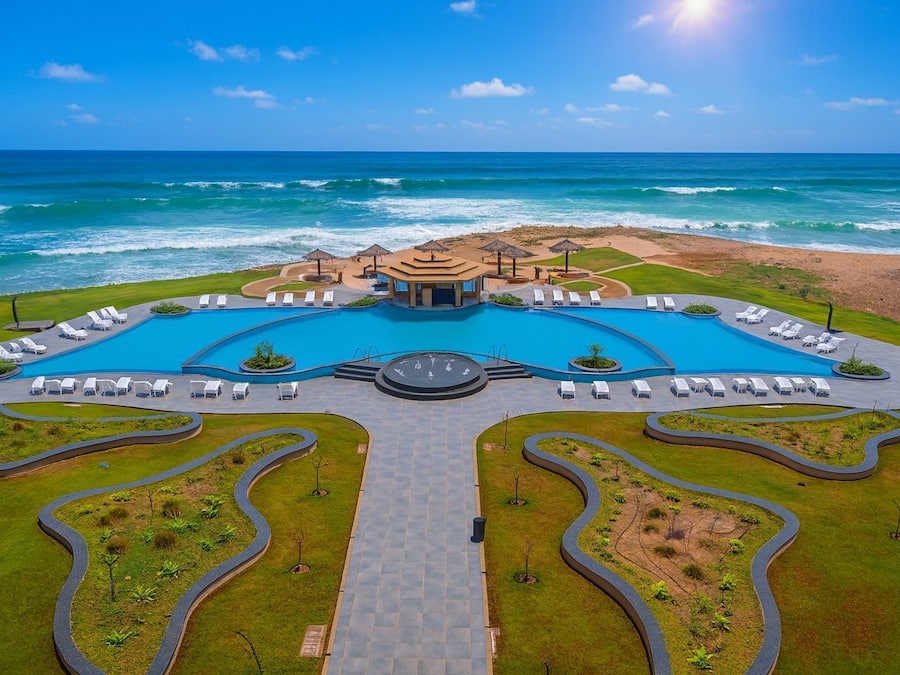 Een resort met een centraal gelegen zwembad, ligbedden en uitzicht op de oceaan.