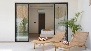 Quarto com duas poltronas de vime, uma cama e porta de vidro deslizante para uma varanda.