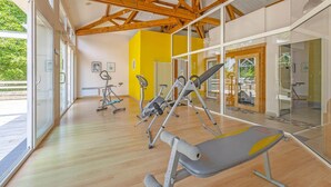 Een sportschool met trainingsapparatuur, grote ramen en een houten plafond.